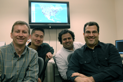 Co-founders of CoBlitz, from left to right: Larry Peterson, KyoungSoo Park, Vivek Pai, and Marc Fiuczynski. Behind them is a map showing the geographic distribution of University Channel downloads through CoBlitz. (Photograph by Mark Czajkowski) CoBlilz founders