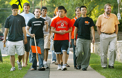 Todd Dale (holding orange sign), a senior majoring in chemical engineering, leads freshmen to a meeting with their advisor. Thanos Panagiotopoulos (right), professor of chemical engineering, walks with the group. (Photo by Frank Wojciechowski) Thanos Panagiotopoulos walkd with members of this year's incoming class